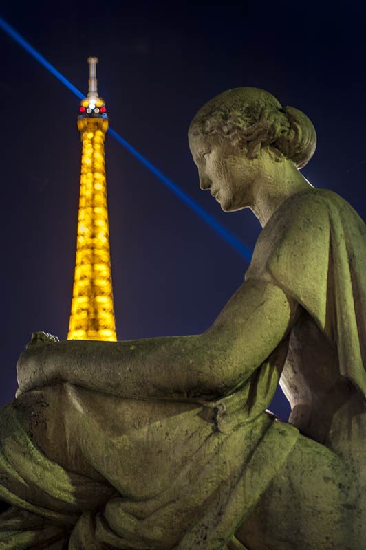 Particolare della torre eiffel dietro ad una statua di donna